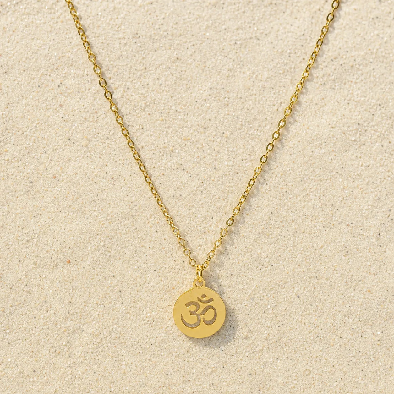 OM Kette Gold auf hellem Sand